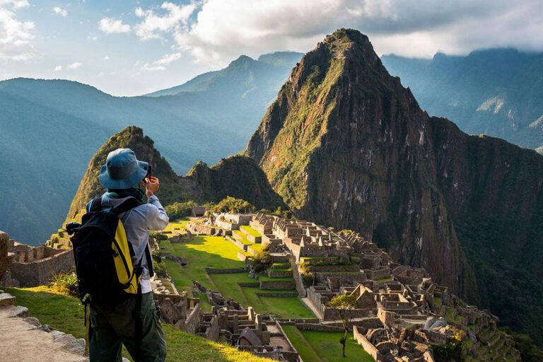 Tourist photographing Machu Picchu with Huayna Picchu mountain in the background.